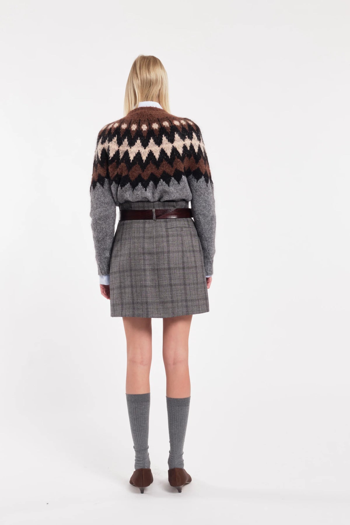 Person wearing a patterned sweater and plaid skirt on a white background