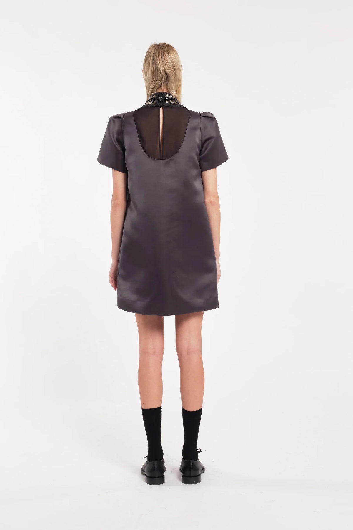 Person wearing a dark gray dress with a unique back design on a white background