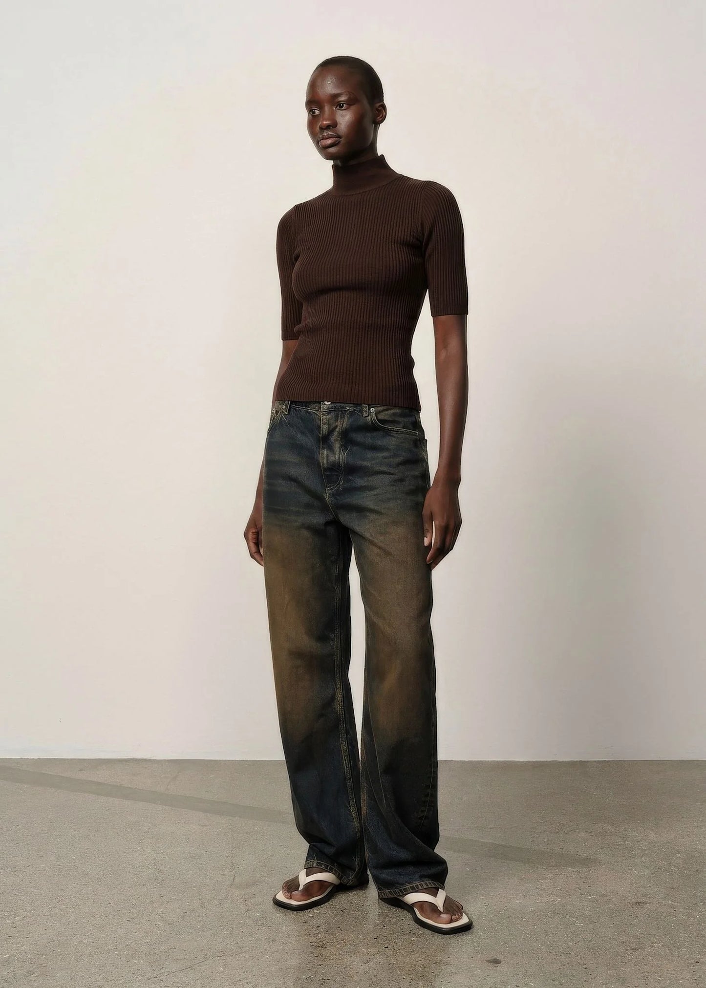 Person wearing a brown turtleneck and jeans standing against a plain background