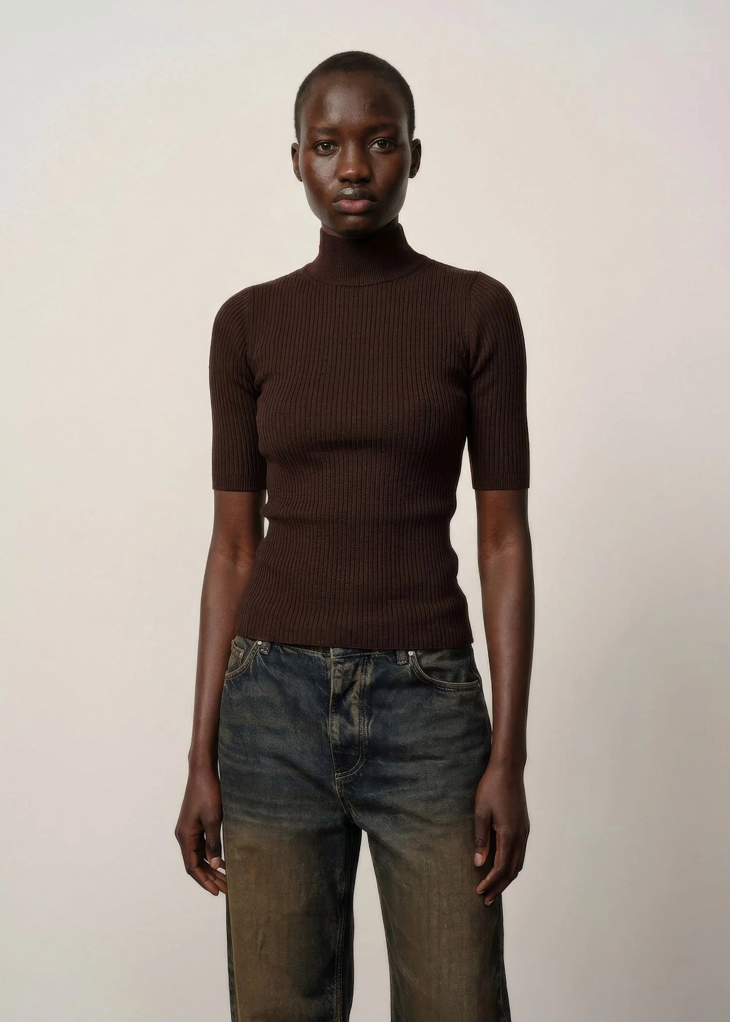 Person wearing a brown ribbed turtleneck and jeans against a plain background