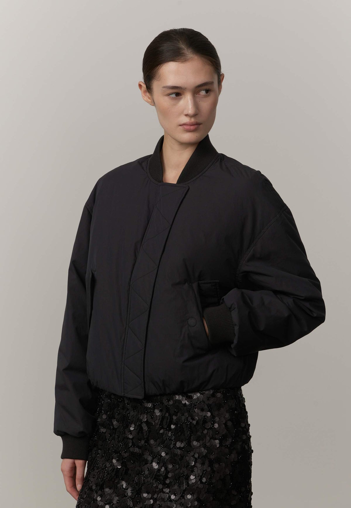 Person wearing a black jacket and black sequin skirt against a plain background