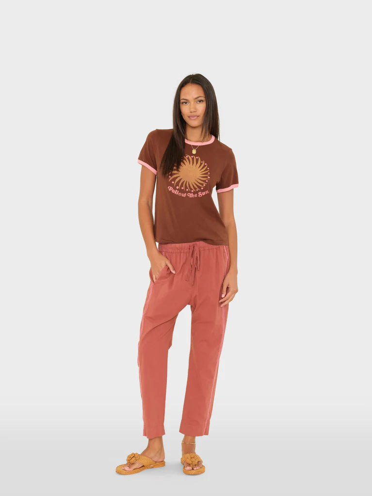 Woman wearing a brown t-shirt with a sun design and pink pants on a white background