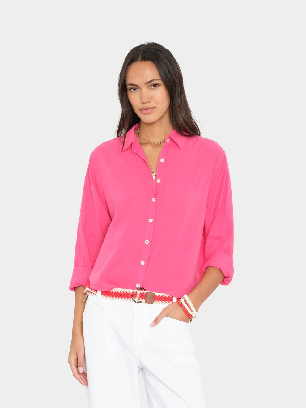 Woman wearing a bright pink shirt and white pants on a light gray background