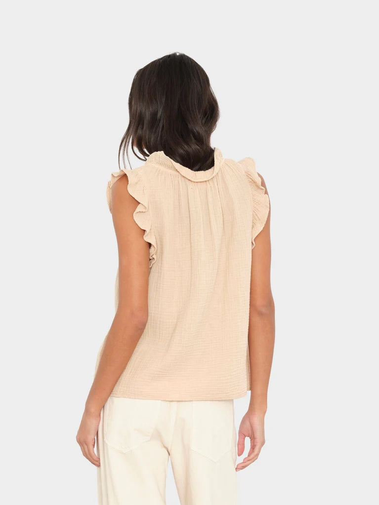 Woman wearing a beige sleeveless top with ruffled details on a white background