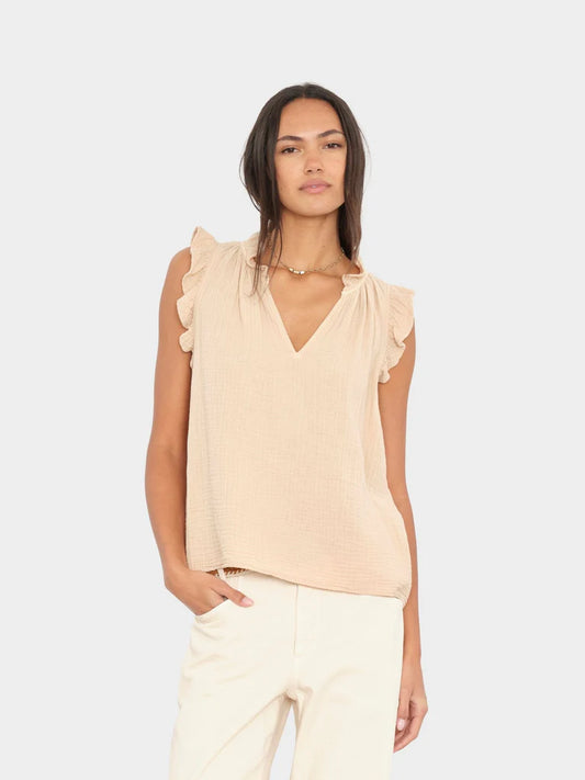 Woman wearing a beige sleeveless top with ruffled sleeves on a white background