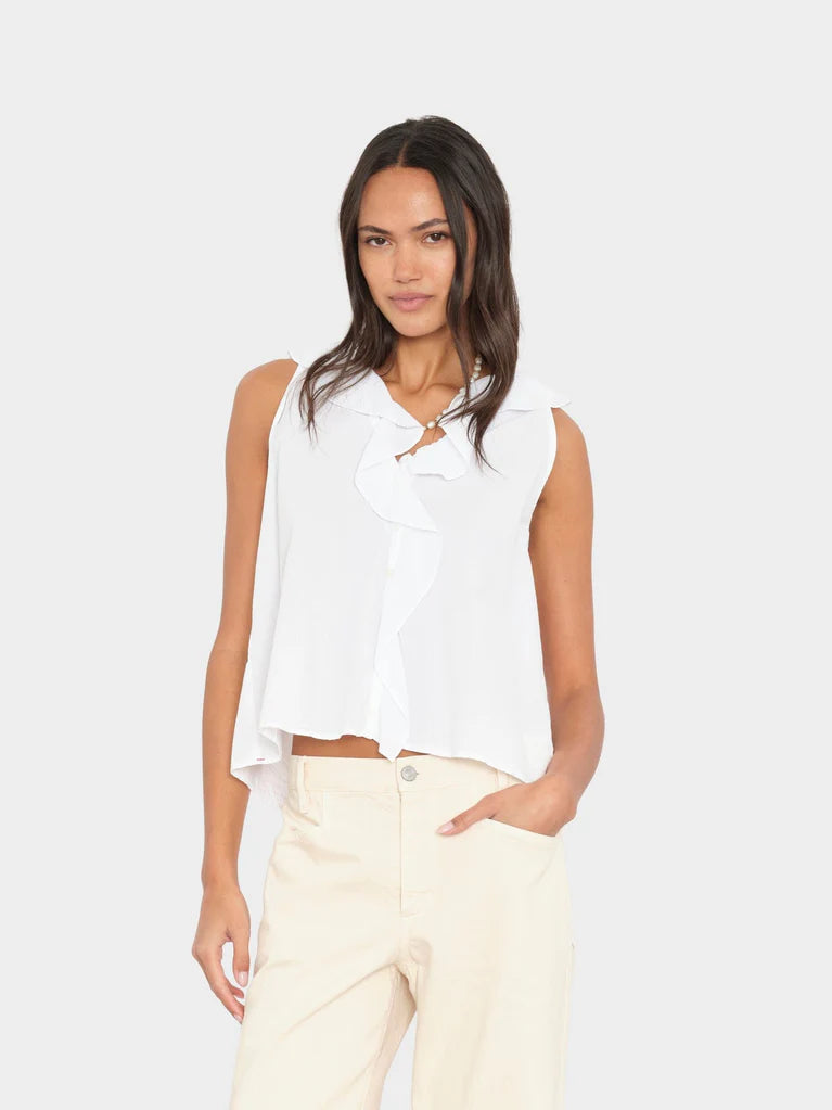 Woman wearing a white sleeveless blouse and beige pants on a light gray background